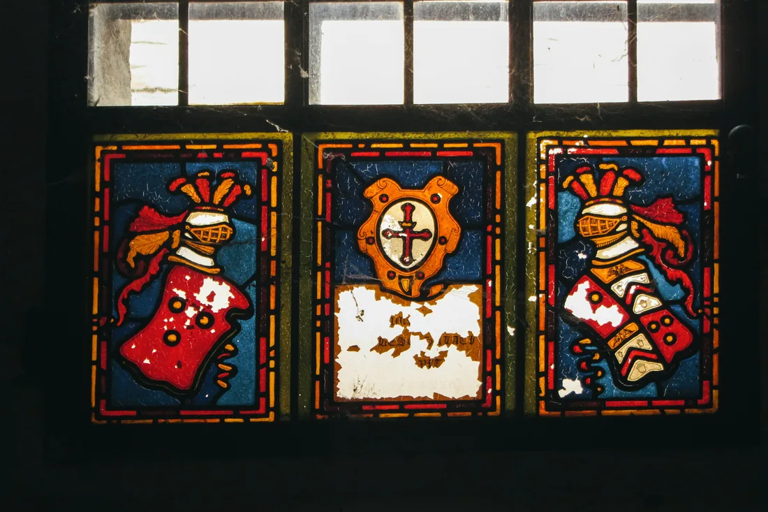 Panel emplomado de tres compartimentos con escudos heráldicos pintados sobre vidrio azul, rojo y ámbar, visto a contraluz